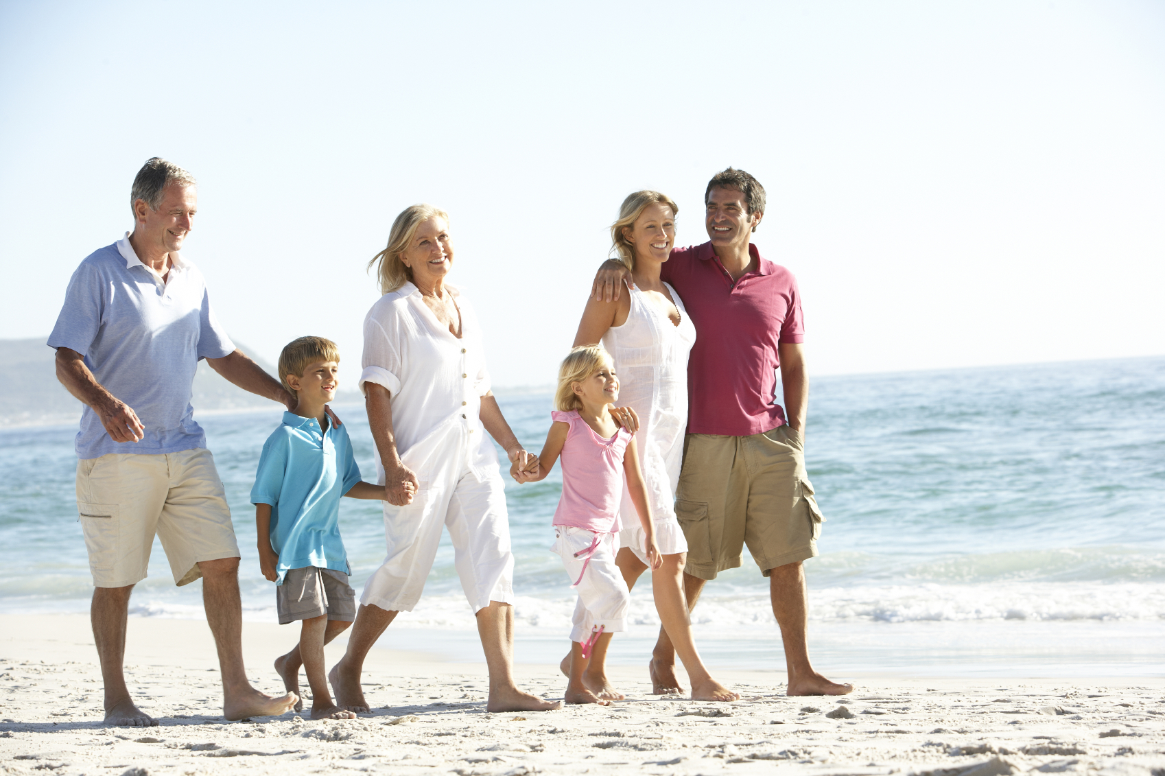Three Generation Family On Holiday Walking On Beach